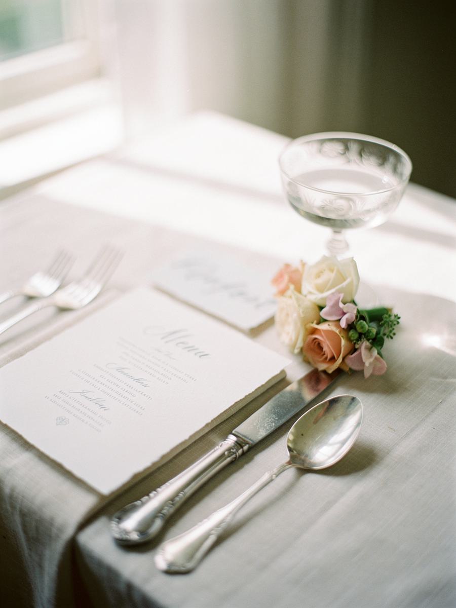 A wedding place setting with a letterpress menu card, antique silver cutlery and a posy of garden roses
